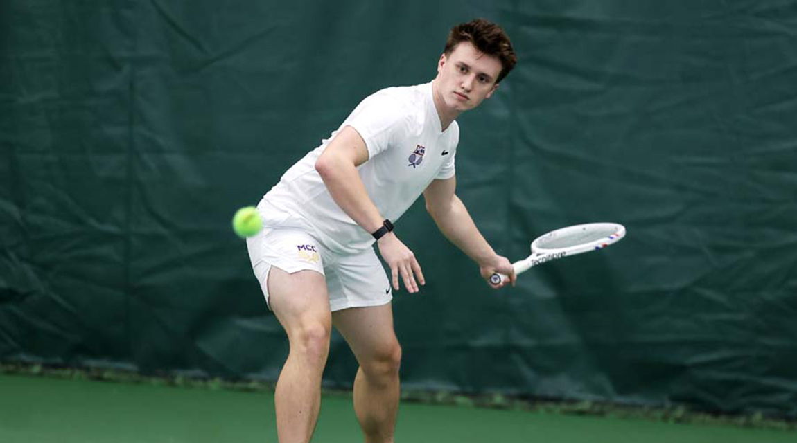 A men's tennis player is preparing to return a shot on an indoor tennis court. 